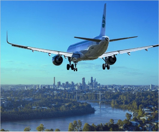 An aerospace marvel, the airplane approaches a city skyline above a river with trees and bridges visible below, under a clear blue sky.