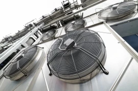 Close-up view of multiple large industrial ventilation fans mounted on a building exterior. These industries-grade fans are enclosed in metal cages and aligned in a vertical arrangement.