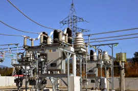 An outdoor electrical substation, pivotal to various industries, features transformers, circuit breakers, and power lines set against a clear blue sky.
