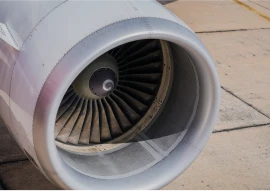 Close-up of an aircraft jet engine on an airplane parked on a tarmac, showing the turbine blades inside the circular casing.
