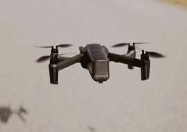 A sleek black drone, an impressive feat of aerospace engineering, gracefully flies over the concrete surface with its four propellers humming in harmony.