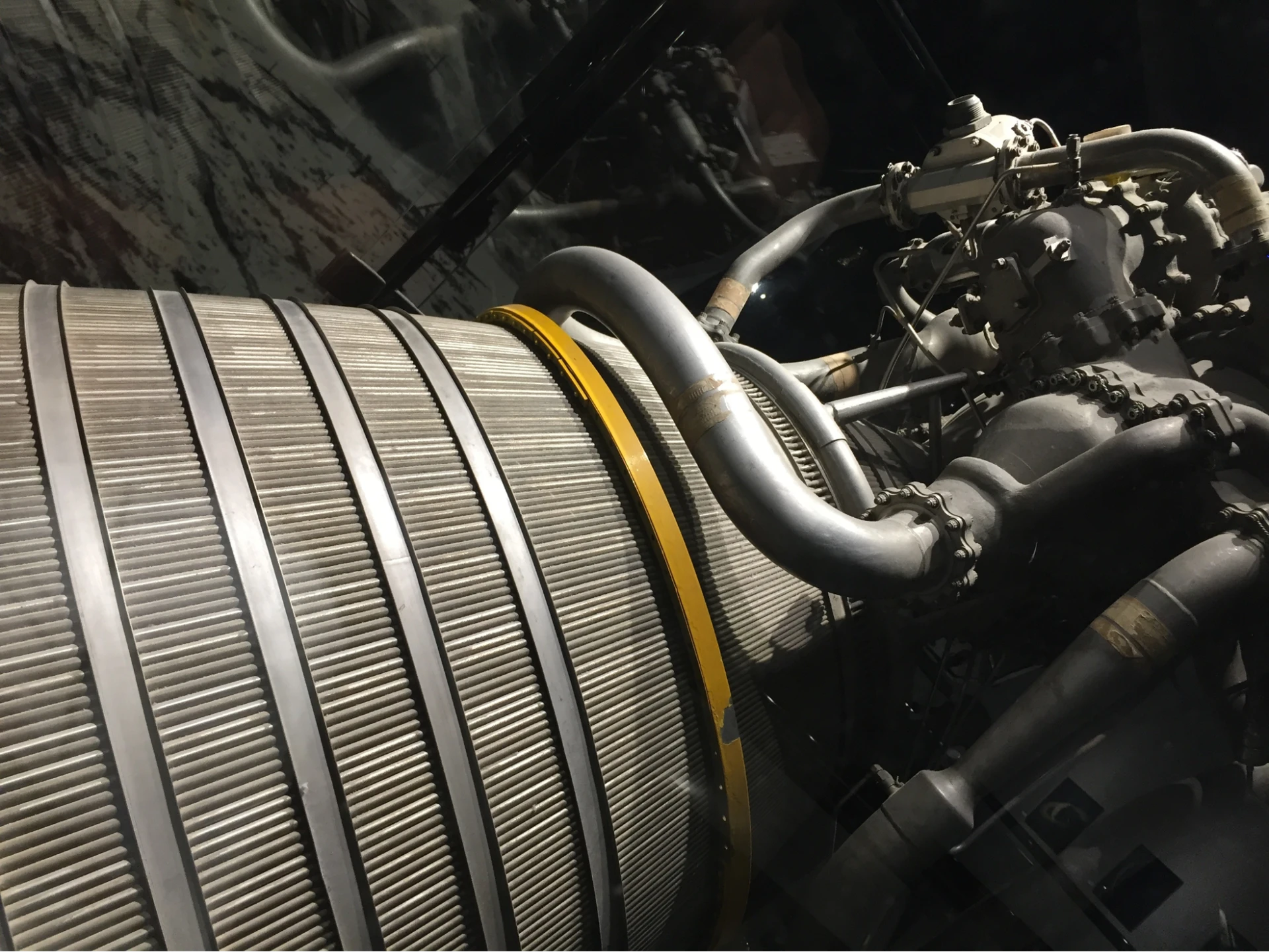 Close-up of mechanical components featuring cylindrical elements, pipes, and connectors with a yellow band, set against a dark background.