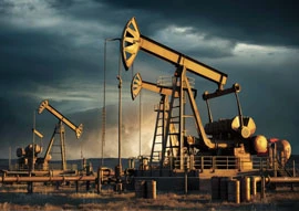 Several oil pumpjacks, showcasing the advancements in oil & gas technology, stand in a field under a dramatic, cloudy sky.