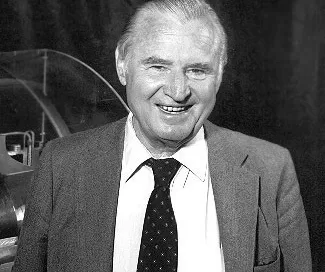 A smiling elderly man in a suit and tie stands confidently before a dark backdrop, embodying the wisdom and expertise associated with Softinway's turbomachinery innovations.