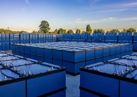 Rows of large blue batteries, showcasing renewable energy technology, are arranged outdoors under a clear sky.