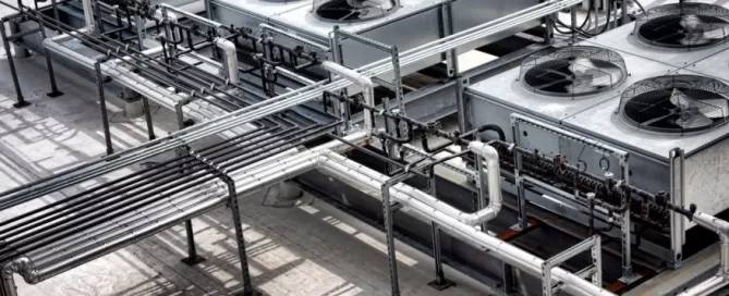 Rooftop industrial HVAC system with multiple large fans and interconnected metal pipes on a concrete surface.