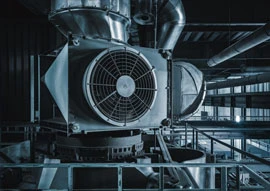 In a dimly lit factory setting, a large industrial ventilation fan hums alongside intricate HVAC & Refrigeration systems, intertwining with metal ducts and pipes.