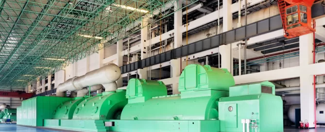 Large green industrial machines inside a spacious facility with a high ceiling and a red crane system overhead.
