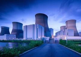 A nuclear power plant dedicated to efficient power generation features cooling towers and industrial buildings silhouetted against a dusk sky.
