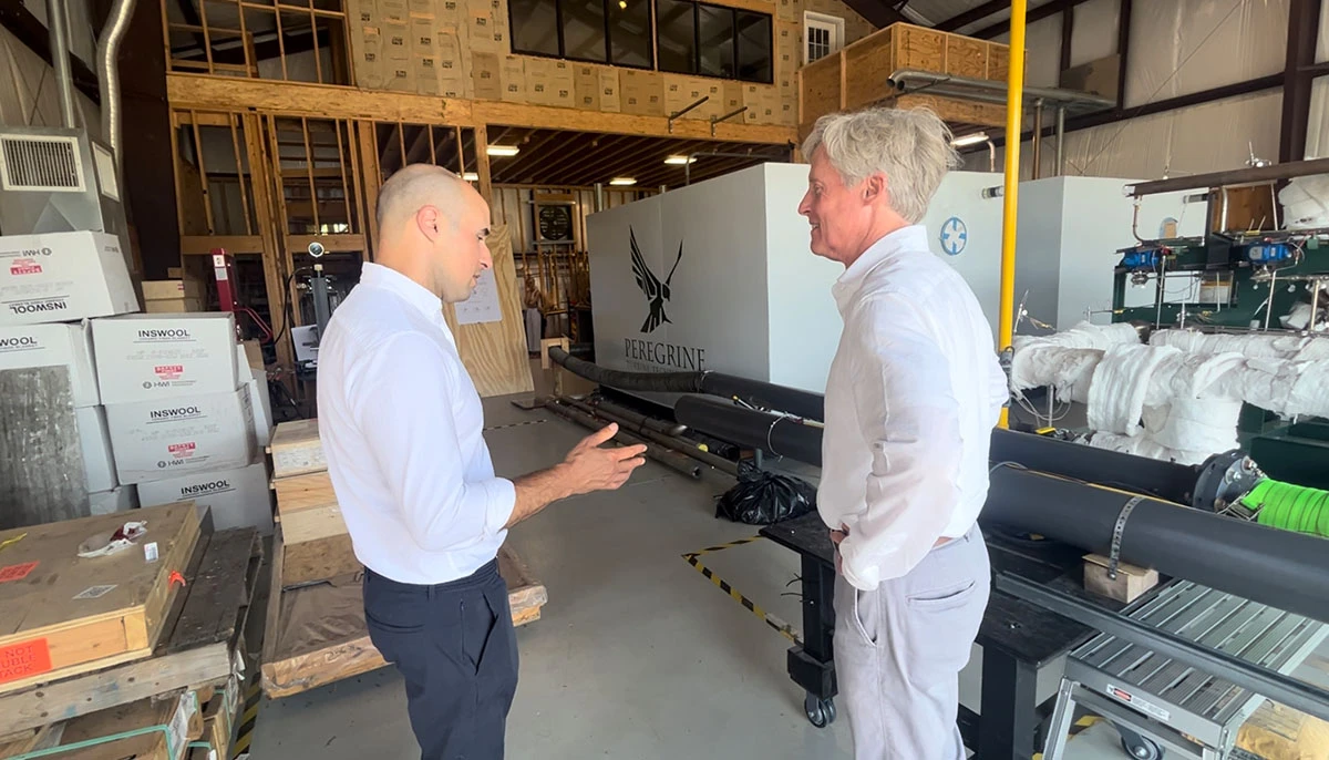 Two men in a warehouse engaged in conversation about turbine design, surrounded by industrial equipment and materials.