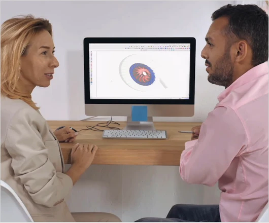 Two people sit at a desk discussing a 3D turbomachinery design displayed on a computer monitor, exploring its potential for development and commercialization.