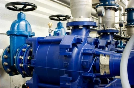 Blue industrial pumps with valves and pipes are expertly installed in a mechanical room, embodying the latest in turbomachinery development. These installations are set to enhance performance and reliability as part of our comprehensive commercialization services.