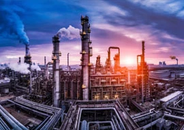 A large industrial refinery, showcasing advanced oil and gas technology, features numerous chimneys emitting smoke against a dramatic sunset sky.