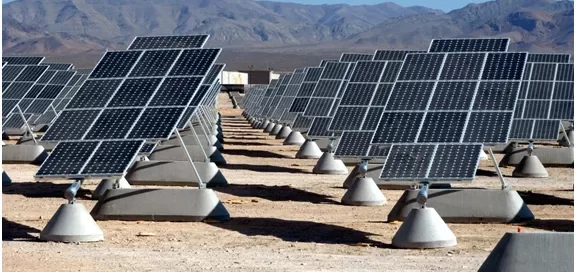 Rows of solar panels in a desert setting with mountains in the background.