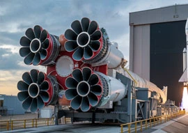 A large rocket booster on a launch pad with multiple engines, showcasing cutting-edge technology, is prepared for launch, set against a partially cloudy sky and industrial buildings in the background.