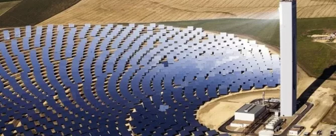 Aerial view of a solar power tower surrounded by an array of solar panels in a rural landscape.