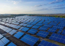 A large solar farm featuring advanced renewable energy technology extends across a vast landscape, with rows of solar panels gleaming under a blue sky dotted with scattered clouds.