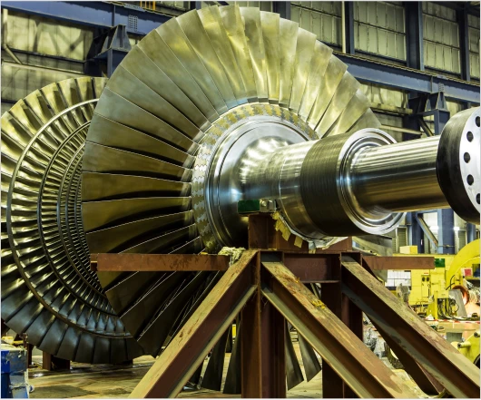 Close-up of a large industrial turbine inside a factory setting, showcasing metallic blades and a central shaft supported by a metal frame, reflecting the latest in turbomachinery development technology.