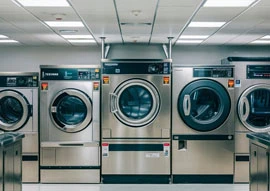 A row of industrial appliances, resembling sleek medical devices, stands in a brightly lit laundromat.