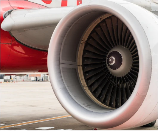 Close-up of a jet engine turbine on an airplane, showcasing state-of-the-art technology, parked on the tarmac with part of the aircraft's red and white fuselage visible.
