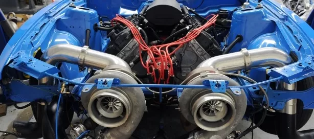 Car engine with red wires and two large turbochargers installed, displayed in a blue vehicle frame.