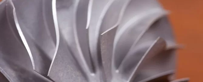Close-up of a metal turbine blade with sharp, curved edges and a shiny surface.