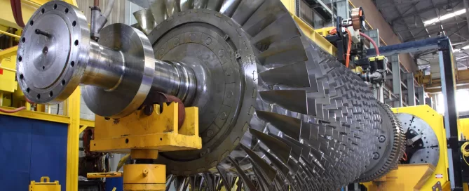 Large industrial turbine in a factory setting with yellow and blue machinery surrounding it.