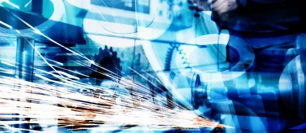 Close-up of sparks flying from a metal being cut in an industrial workshop. Machinery and tools are visible in the blurred background, with a blue tint overlaying the scene.
