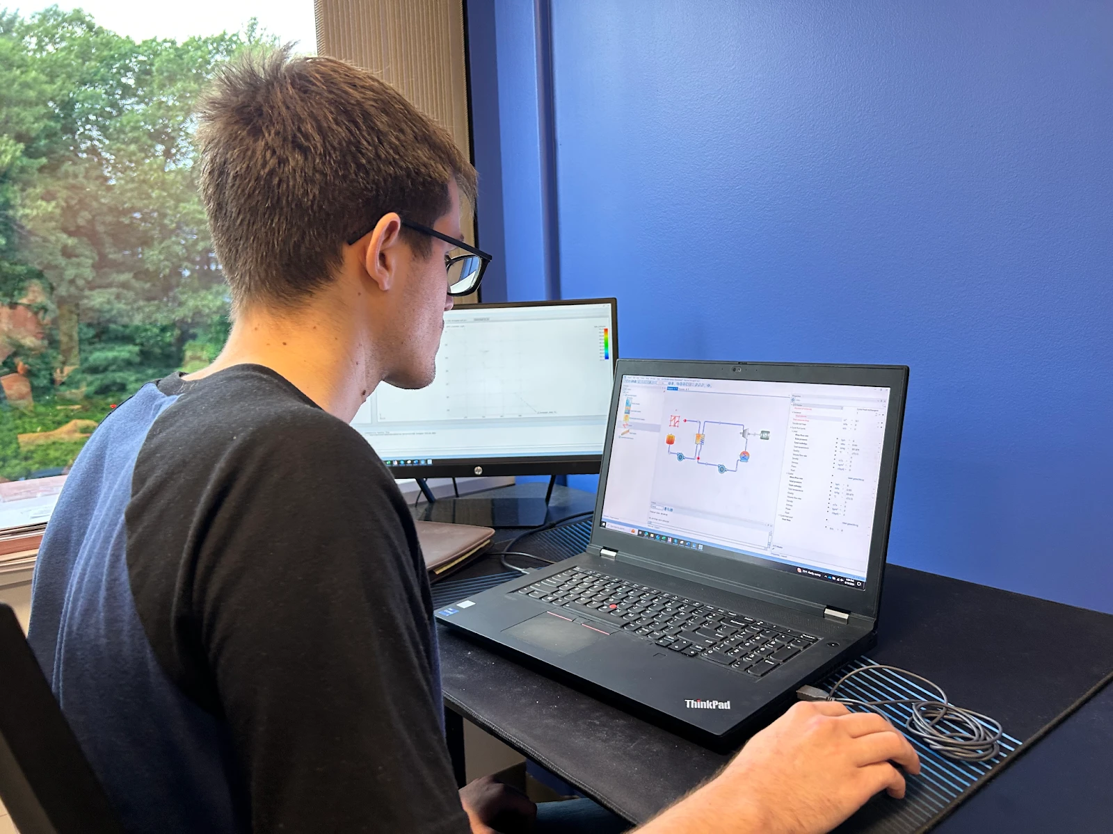 software-customization-2 A person wearing glasses concentrates on customizing electronic circuit design software on a laptop, flanked by another monitor at the desk.
