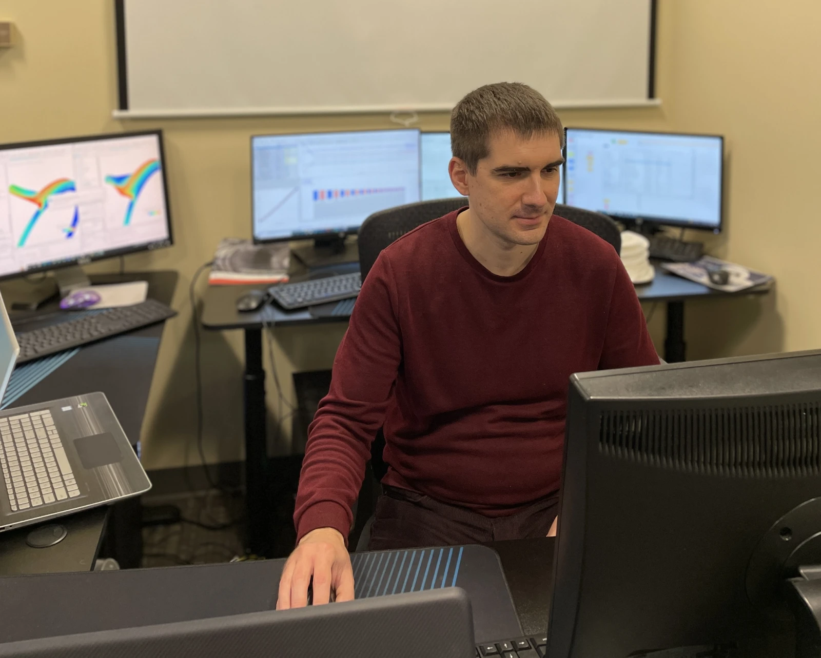 software-customization-3 A person sits at a desk in front of multiple computer monitors displaying technical diagrams and data, meticulously working on intricate software customization to tailor solutions for complex projects.