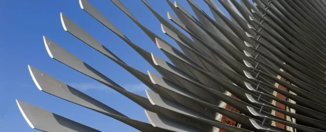Close-up of a modern metal sculpture with long, curved blades against a clear blue sky.