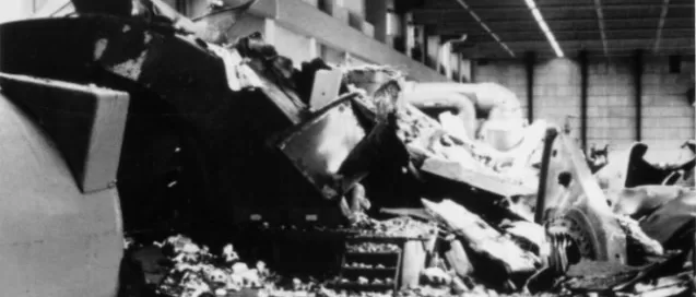 Debris and wreckage fill an industrial building, with large twisted metal pieces scattered on the ground.